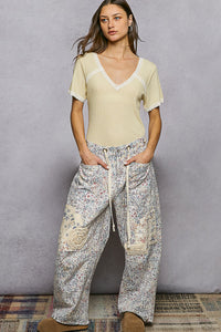 Woman wearing a light-colored top and patterned pants against a gray background