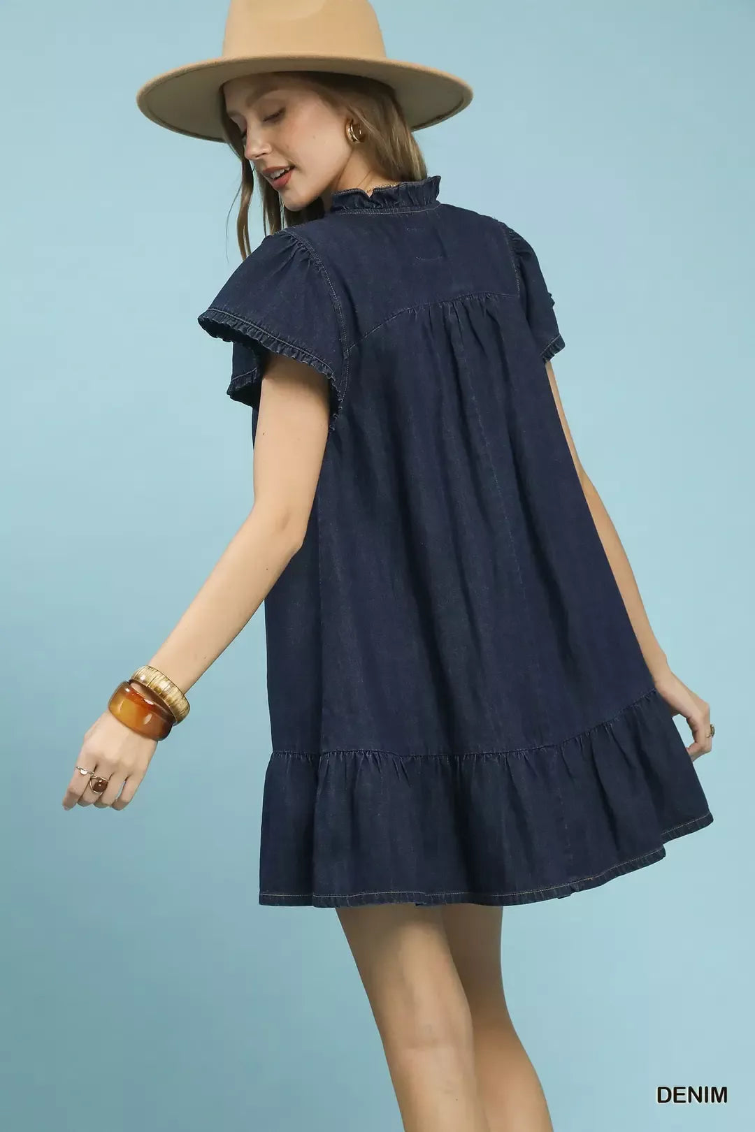 Woman wearing a denim dress and beige hat against a light blue background
