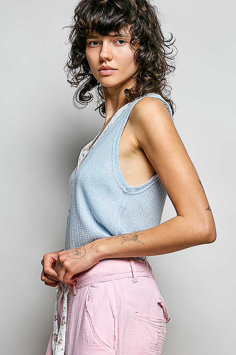 Woman wearing a light blue sleeveless top and pink pants against a plain background