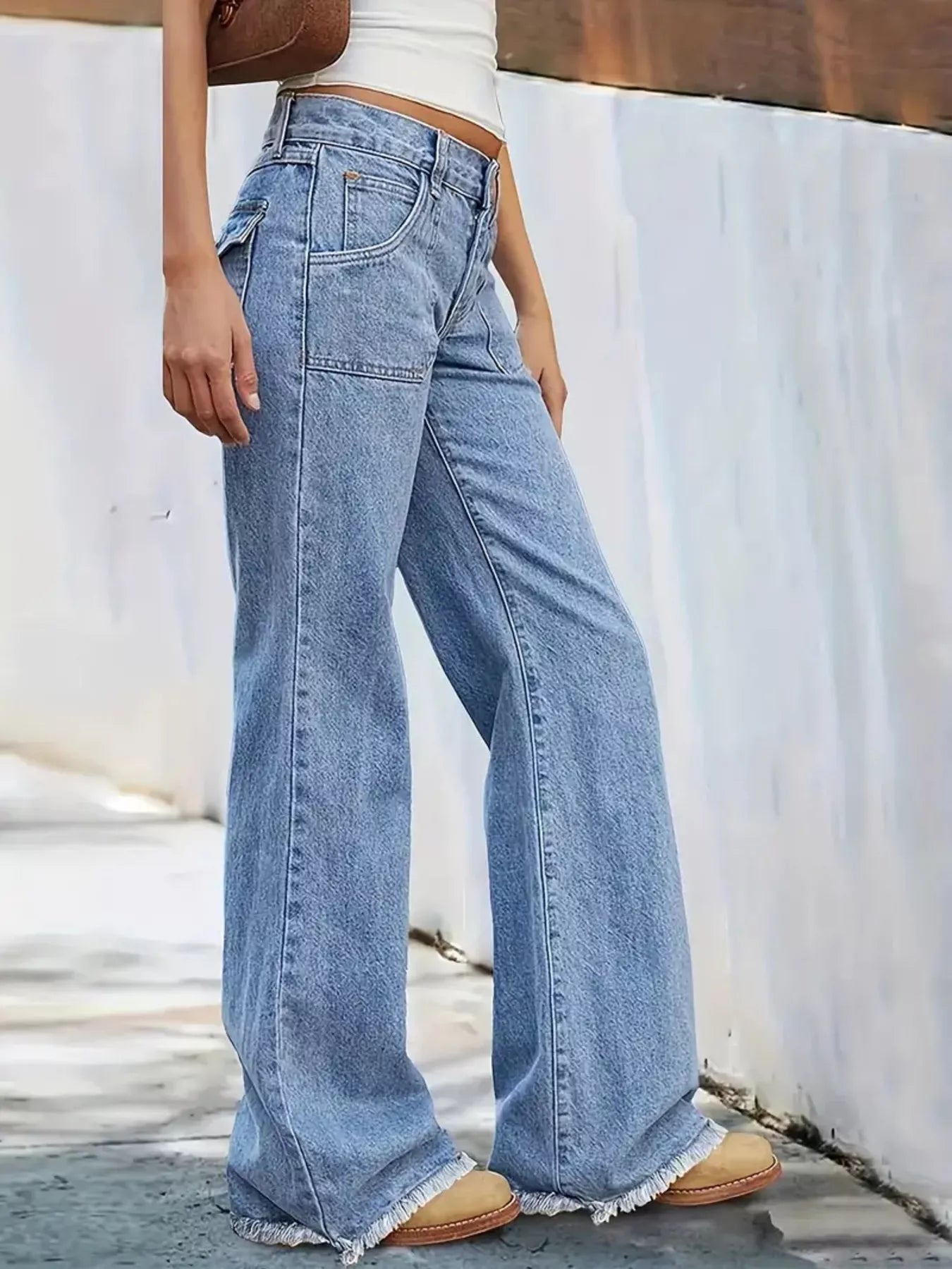 Person wearing light blue wide-leg jeans against a white wall.