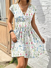 Woman wearing a floral dress standing against a white brick wall.
