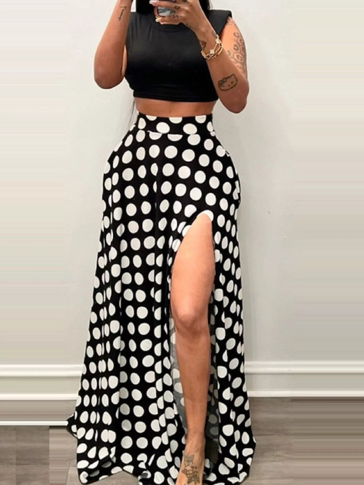 Person wearing a black crop top and polka dot high-waisted pants with a side slit.