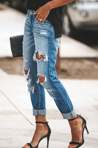 Person wearing ripped blue jeans and black high-heeled sandals with a blurred background.