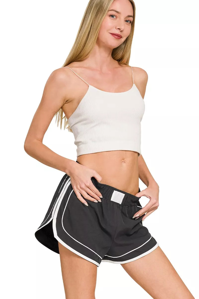 Woman wearing a white crop top and black shorts with white trim on a white background