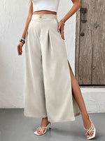 Person wearing beige wide-leg pants with a white top and sandals, standing against a wooden door.