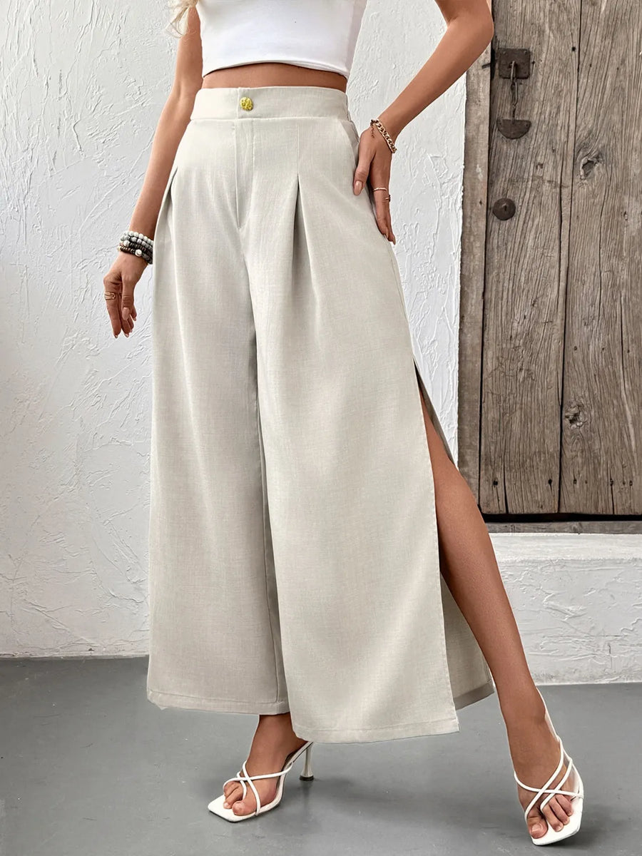 Person wearing beige wide-leg pants with a white top and sandals, standing against a wooden door.