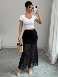 Woman taking a mirror selfie wearing a white crop top and black lace skirt.
