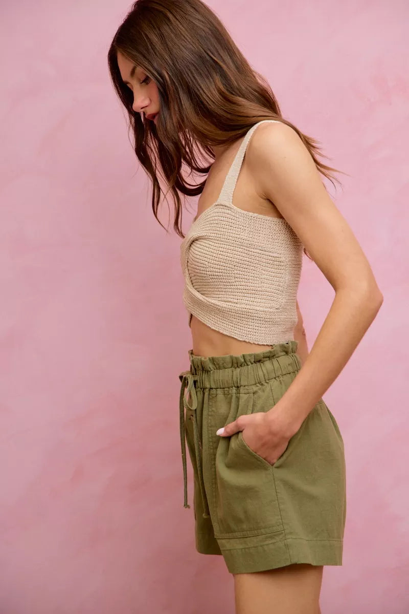 Woman wearing a beige knit top and green shorts against a pink background