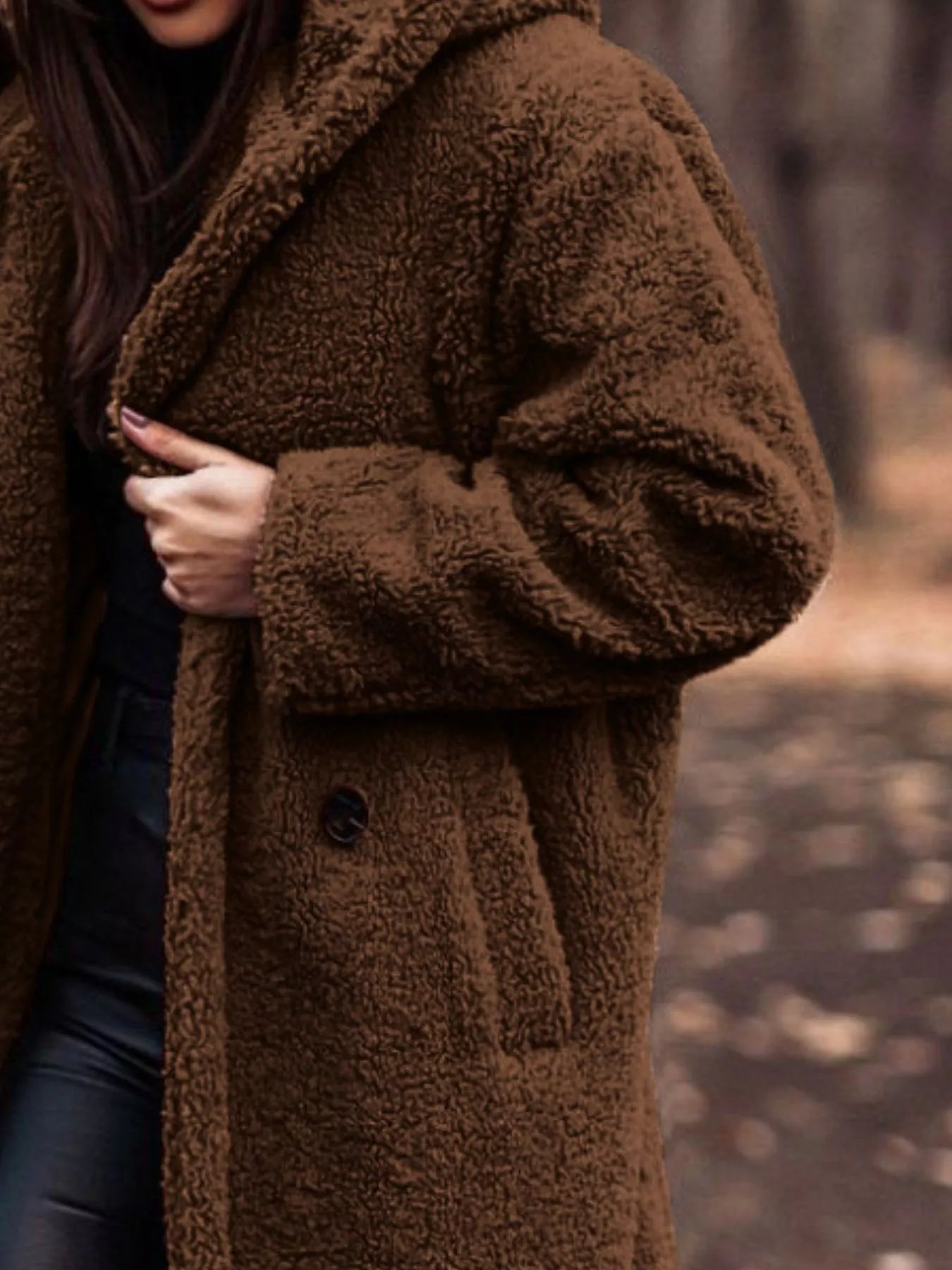 Person wearing a brown teddy coat in a blurred natural setting