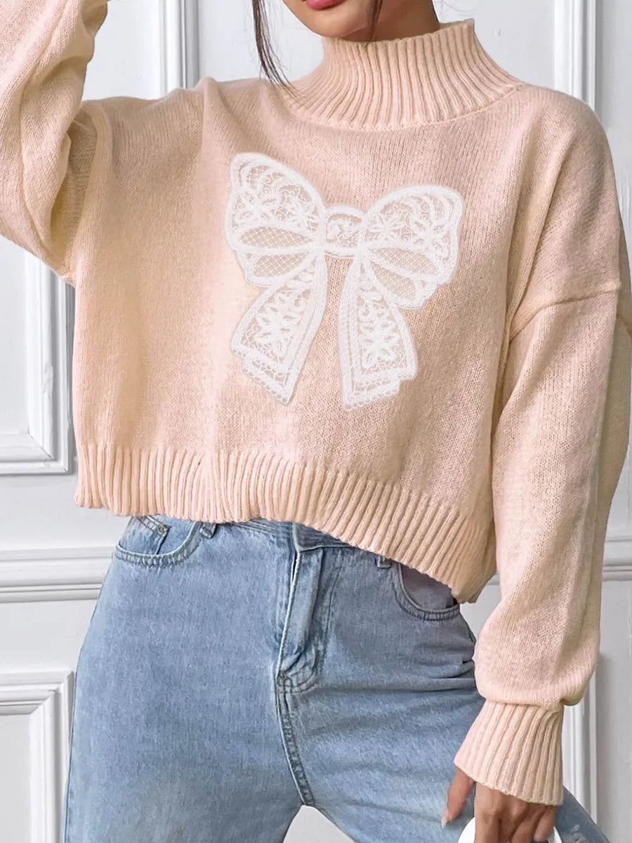 Beige sweater with a white butterfly design worn by a person, against a neutral background.