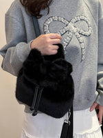 Person holding a black fluffy bag with a gray sweatshirt featuring a decorative bow design.