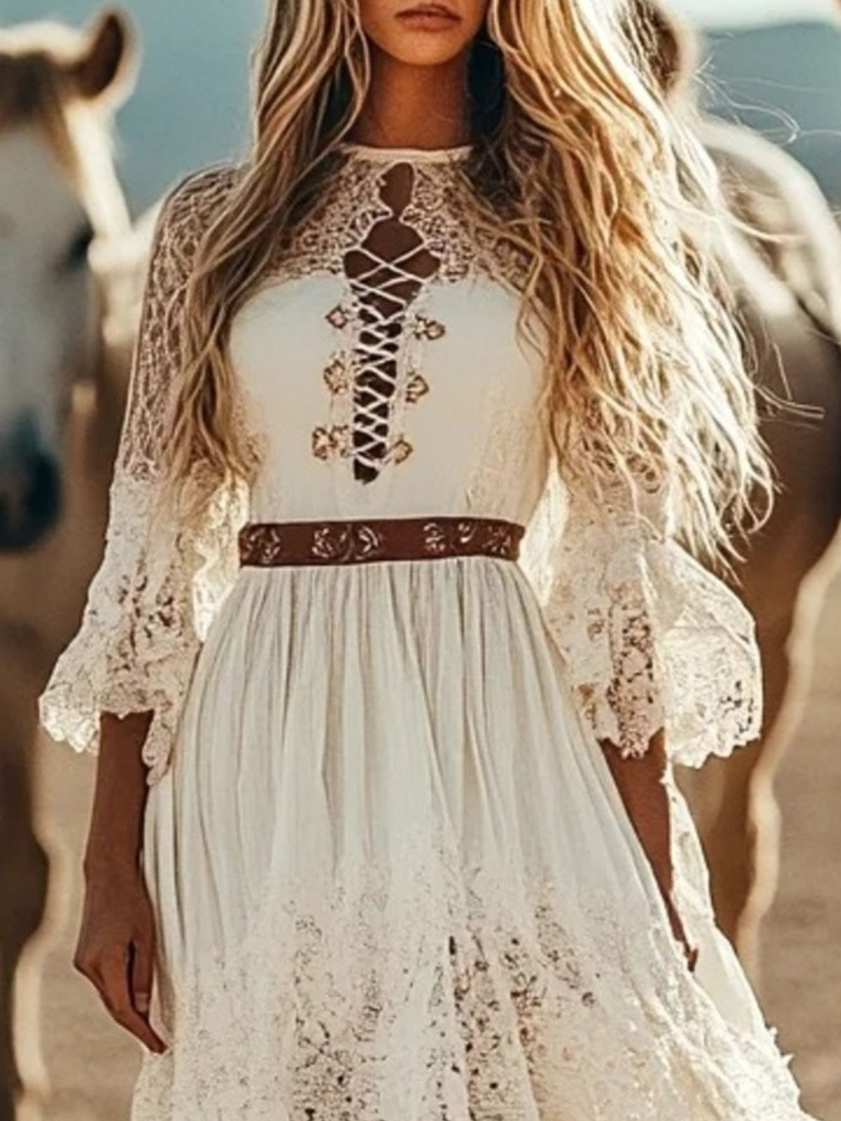 Woman wearing a white lace dress with a brown belt, standing in front of horses.