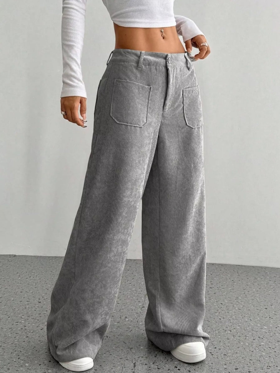 Person wearing gray corduroy pants with a white top against a plain background