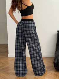 Person wearing black plaid pants and a black crop top on a wooden floor.