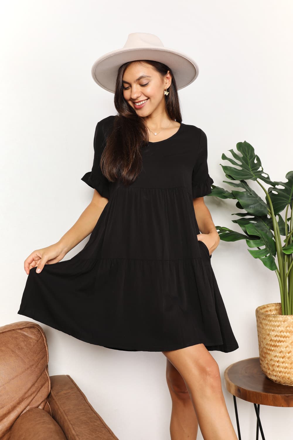 Woman wearing a black dress and white hat in a room with a plant and couch.