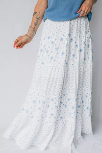 Person wearing a long white floral skirt with a blue top on a light gray background