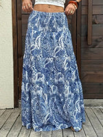 Person wearing a blue paisley patterned skirt on a wooden deck.