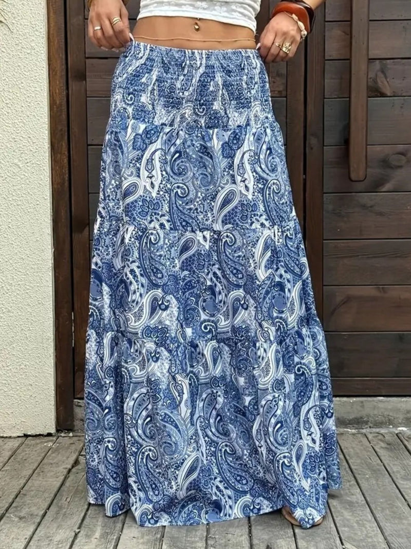 Person wearing a blue paisley patterned skirt on a wooden deck.