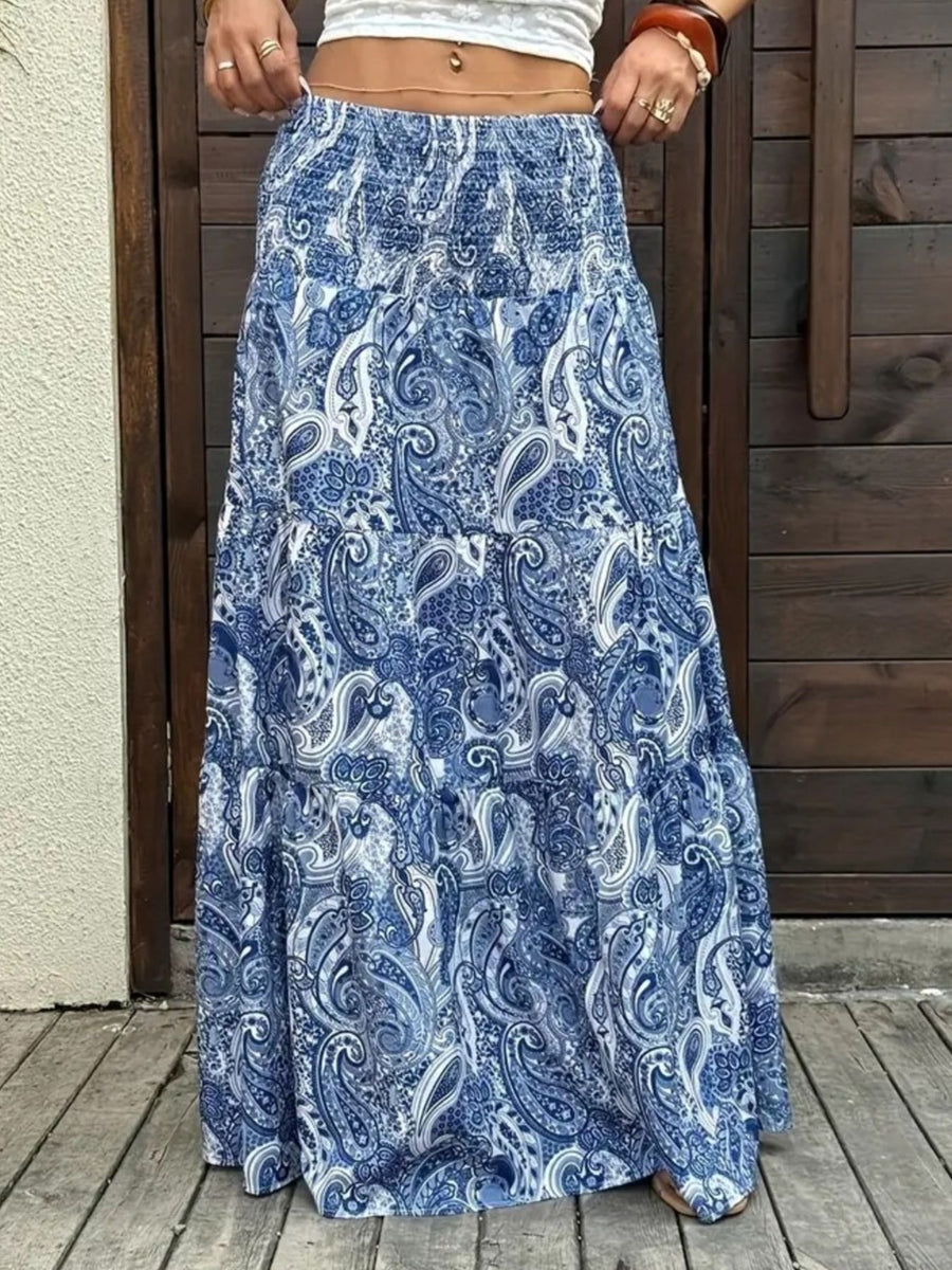 Person wearing a blue paisley patterned skirt on a wooden deck.