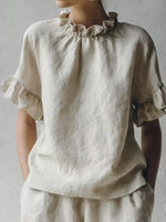 Person wearing a beige blouse with ruffled sleeves against a plain background