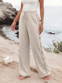 Person wearing beige pants with decorative trim standing on a beach.