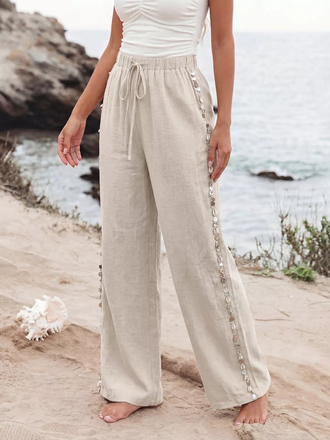 Person wearing beige pants with decorative trim standing on a beach.