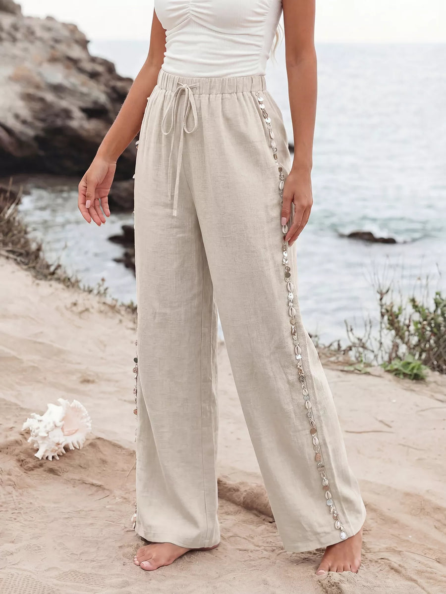 Person wearing beige pants with decorative trim standing on a beach.