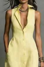 Woman wearing a light yellow sleeveless dress with a plunging neckline against a gray background
