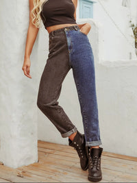 Person wearing a brown crop top, one dark denim jeans leg and one blue denim jeans leg, standing against a white wall.