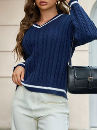 Woman wearing a blue cable knit sweater and white pants, holding a black handbag.