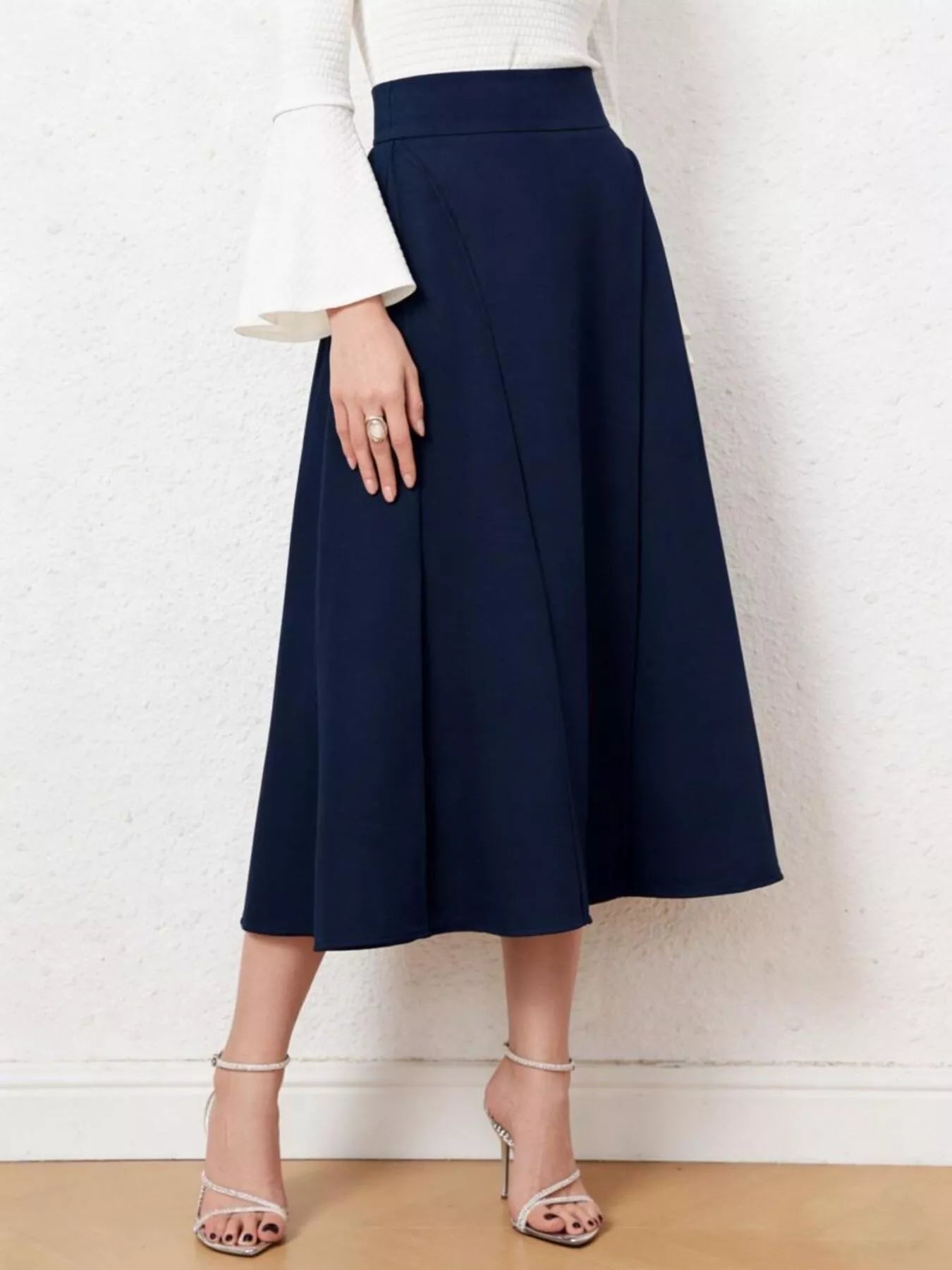 Person wearing a navy blue skirt with a white top against a light background