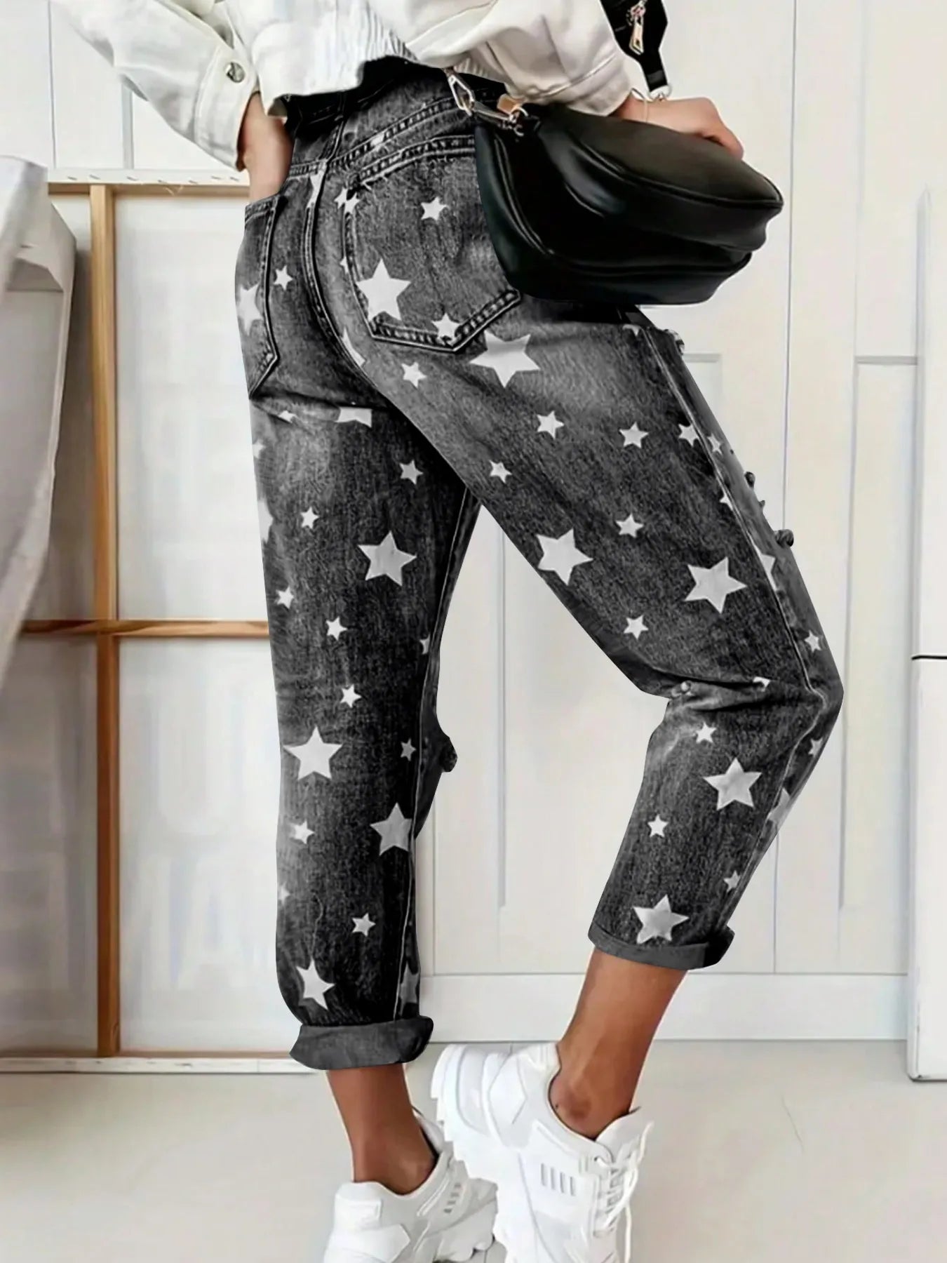 Person wearing star-patterned jeans with a black waist bag indoors.