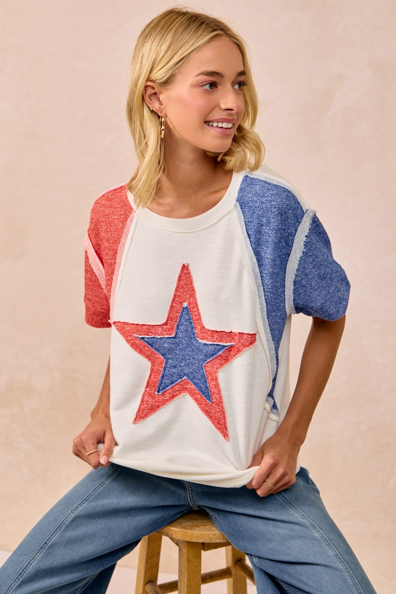 Woman wearing a colorful star-patterned top sitting on a stool against a beige background