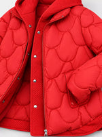 A close-up of a bright red quilted puffer jacket with a hood, featuring a central zipper and silver snap-button closure on a light gray background.