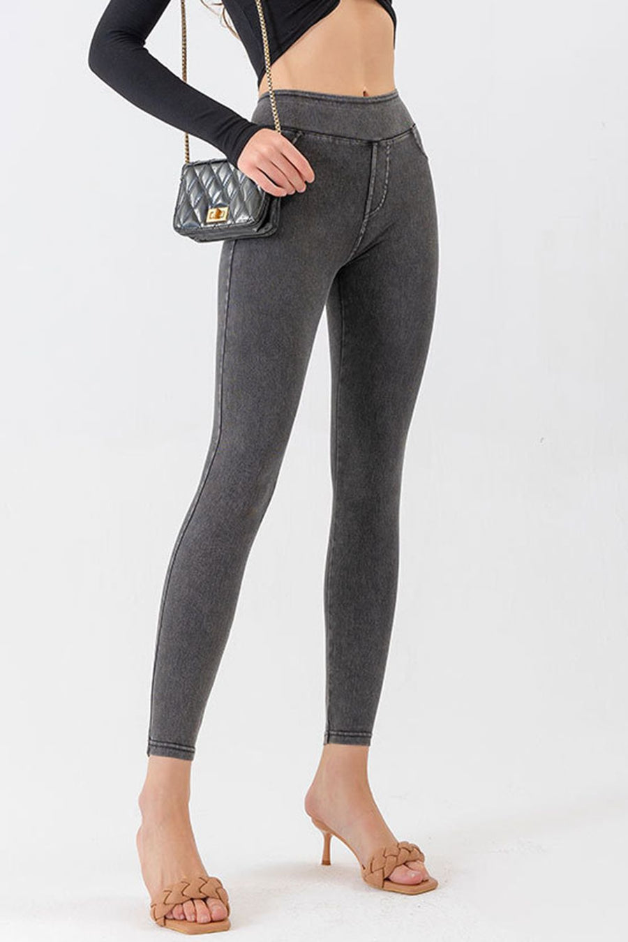 Person wearing gray leggings with a black top and sandals on a white background