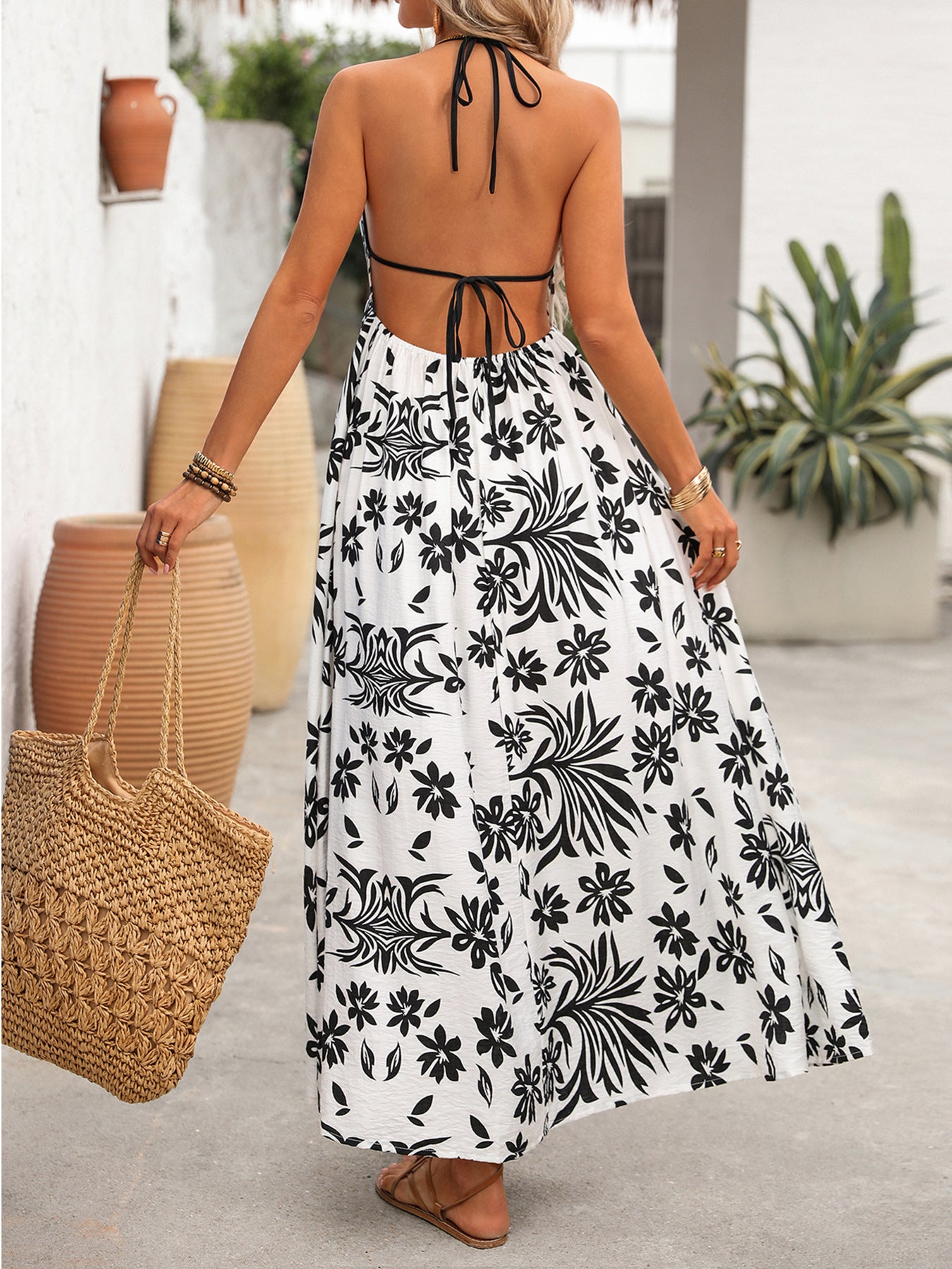 Woman wearing a black and white floral dress holding a woven bag outdoors.