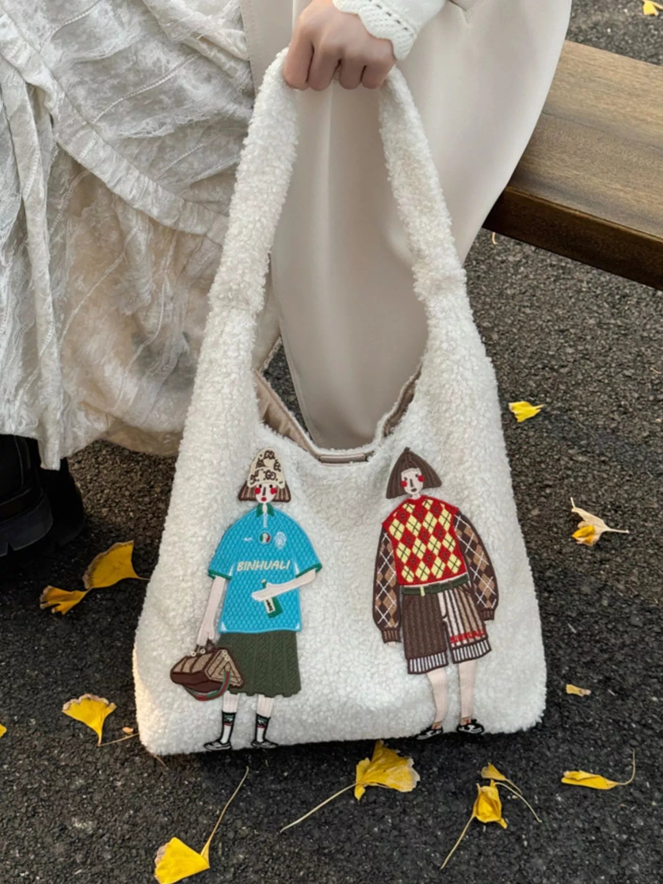 White fluffy bag with embroidered characters on a pavement.