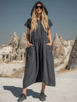 Woman in a long dark gray dress with a hood standing in front of rock formations.