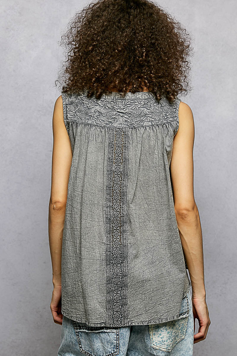 Person wearing a sleeveless gray top with floral embroidery on a plain background