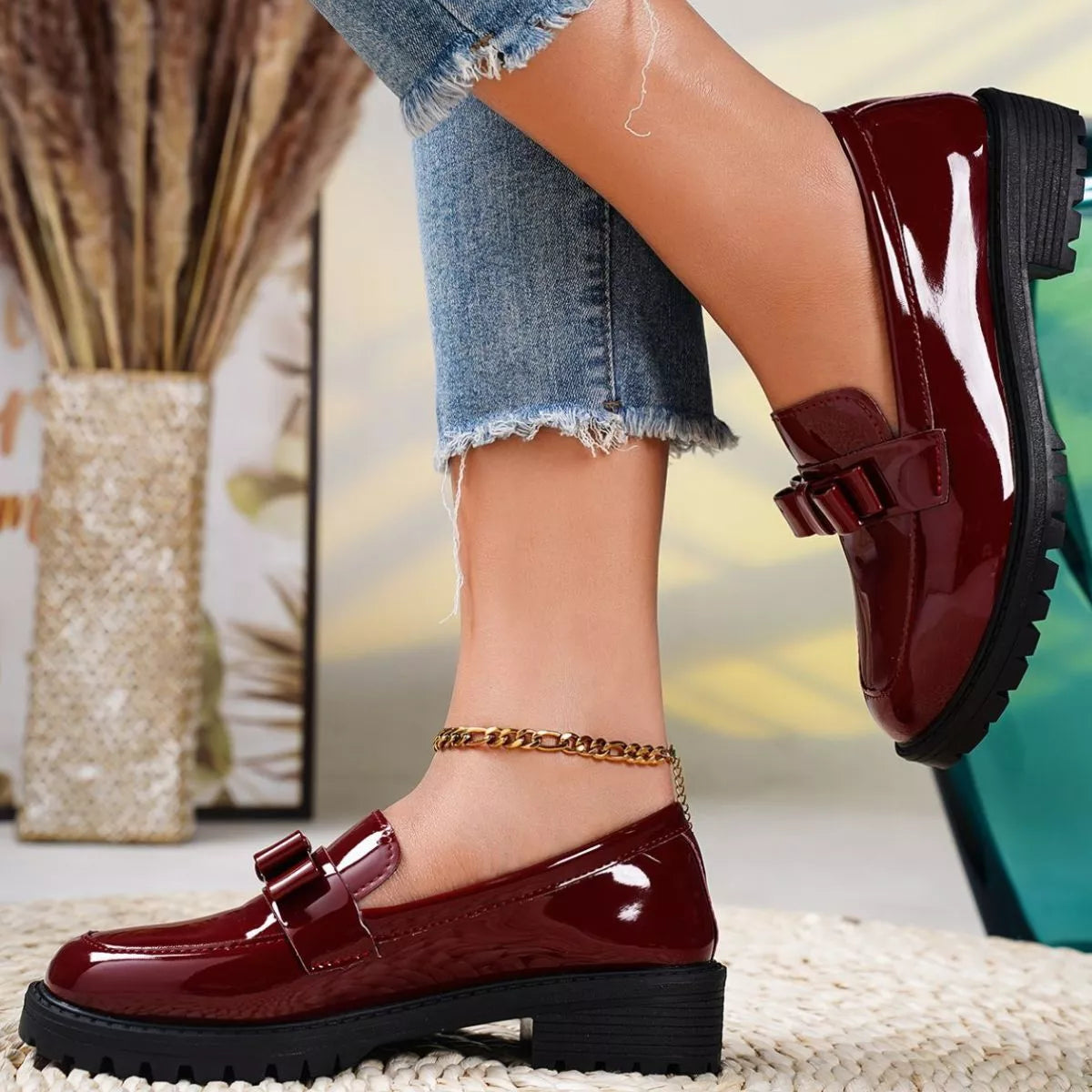 Burgundy patent leather shoes worn with denim shorts on a blurred indoor background