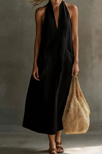 Woman in a black dress holding a beige woven bag against a neutral background