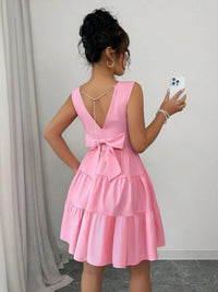Woman wearing a pink dress with a bow detail, taking a selfie.