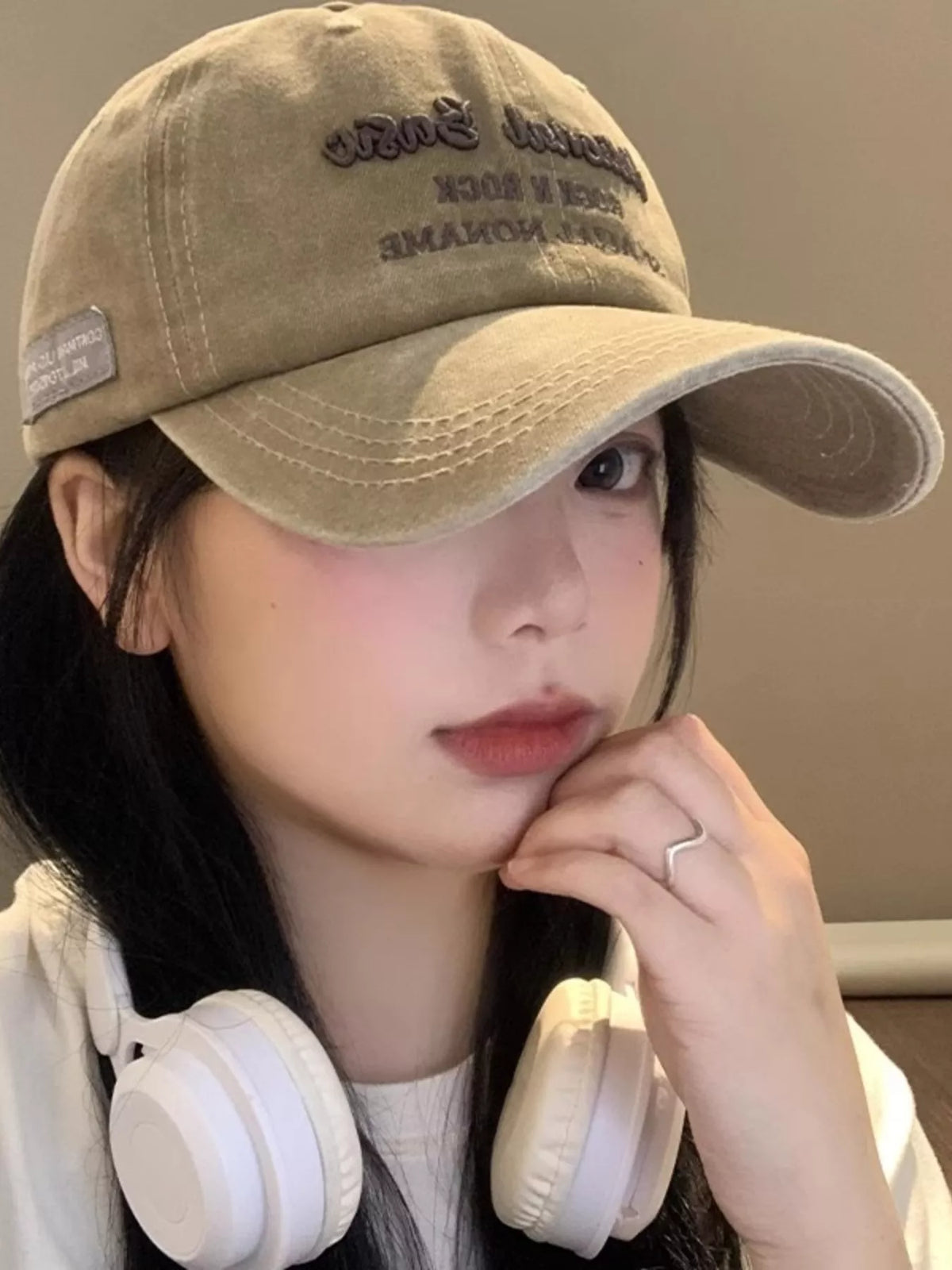 Person wearing a beige cap and white headphones, resting their chin on their hand.