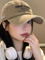 Person wearing a beige cap and white headphones, resting their chin on their hand.