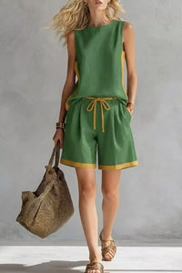 Woman wearing a green outfit with yellow trim, holding a woven bag against a gray background