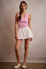 Woman wearing a pink top and white skirt against a plain background