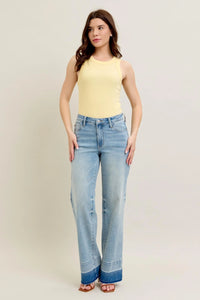 Woman wearing a yellow sleeveless top and blue jeans on a plain background