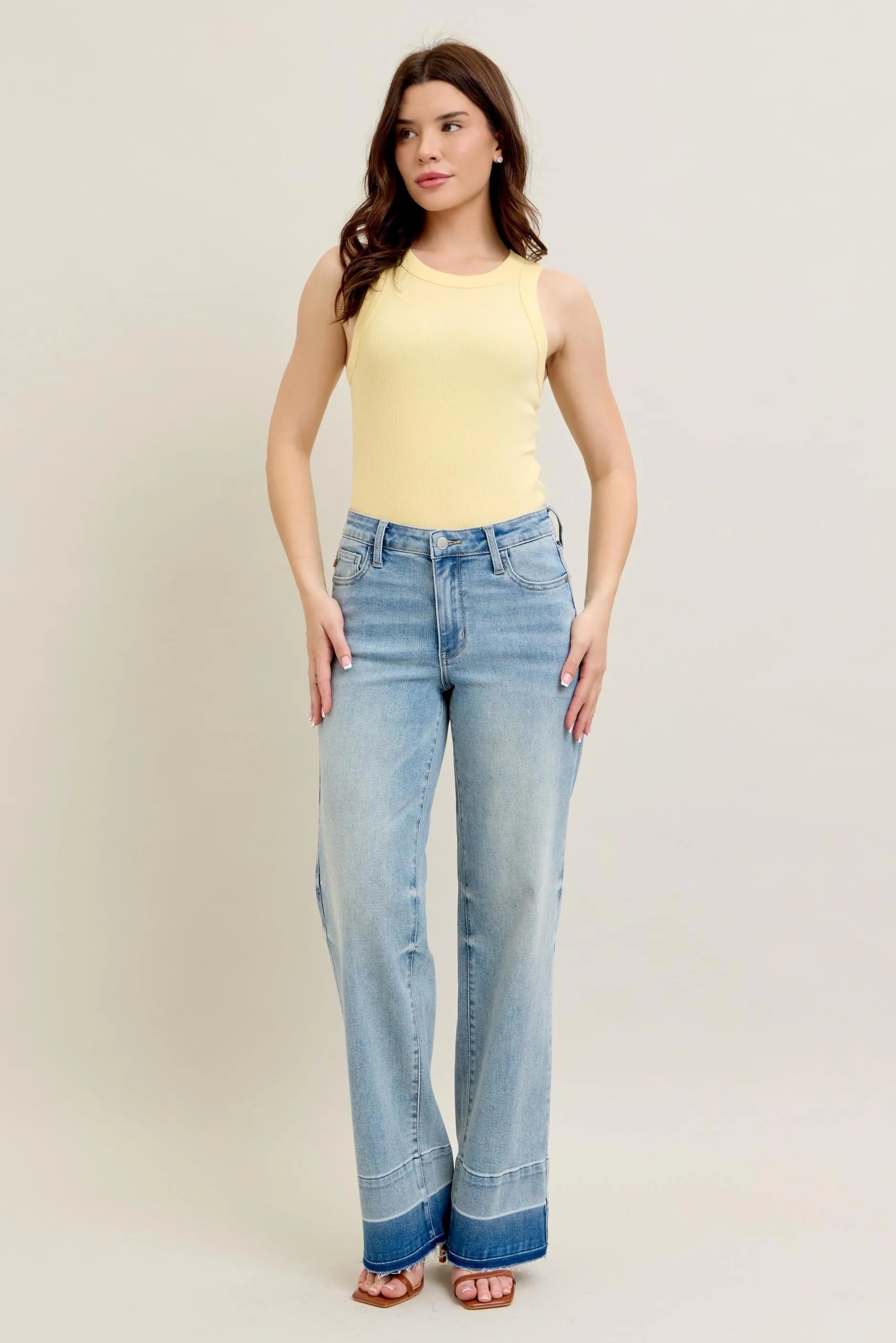 Woman wearing a yellow sleeveless top and blue jeans on a plain background