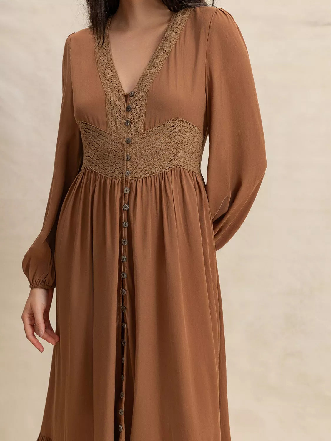 Brown dress with long sleeves and button details on a beige background