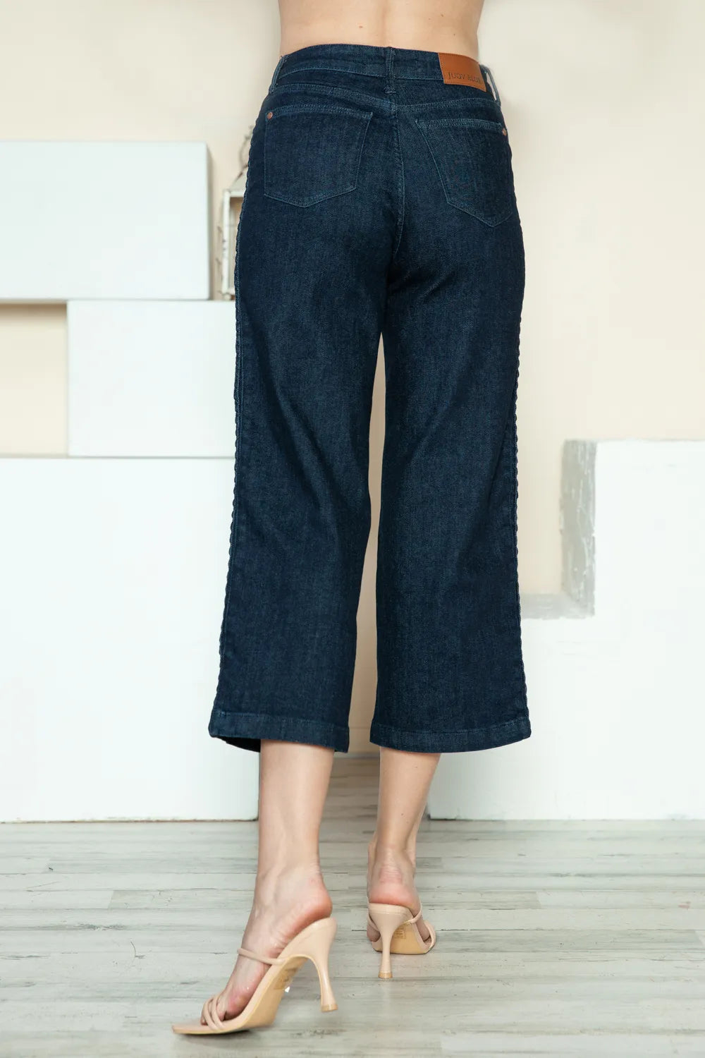 Dark blue jeans worn by a person on a light wooden floor.